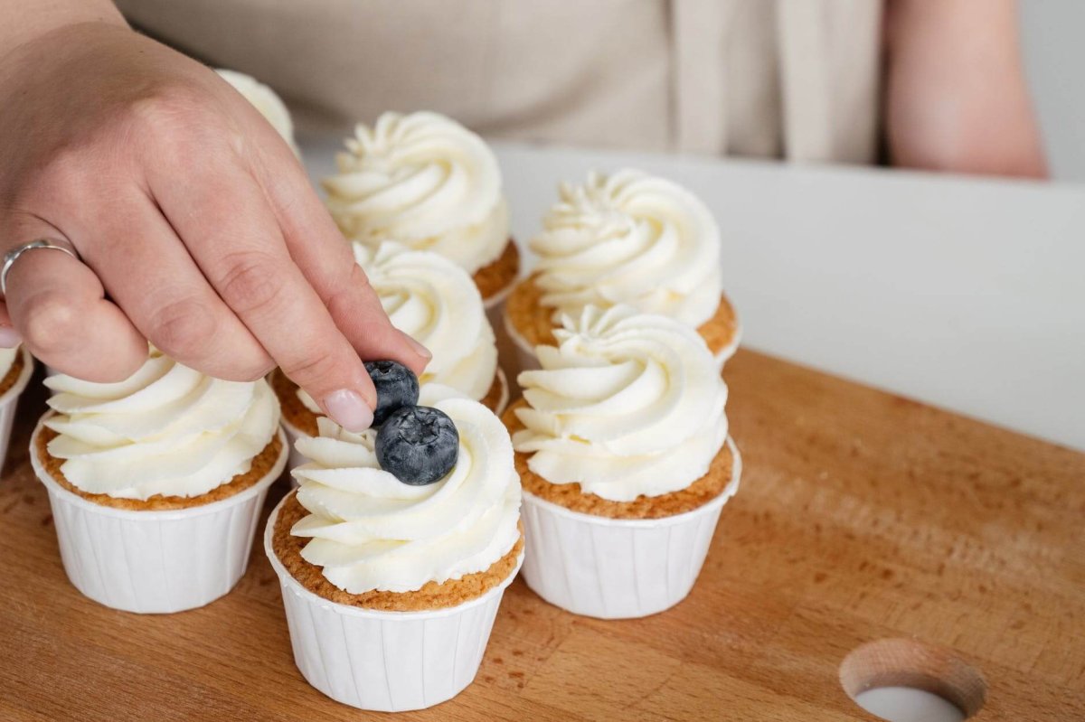 close up shot of a person putting berries on a frosted cupcake
