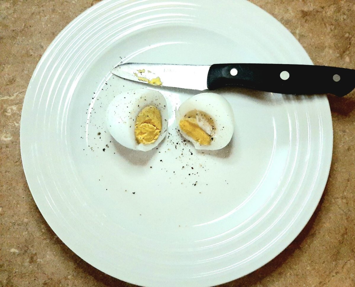 divided, peeled and boiled egg on a white plate with paring knife