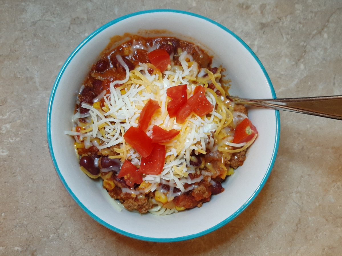 white bowl of Cincinnati-style chili with shredded cheese and diced tomatoes