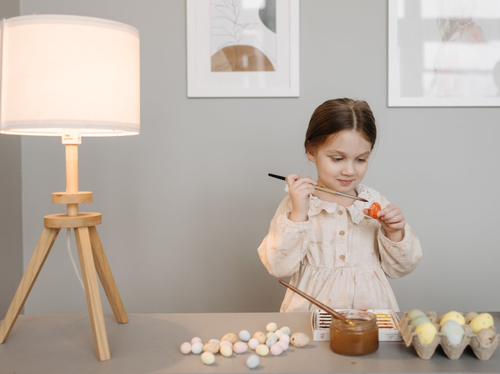 photo of a kid decorating an easter egg near a lamp