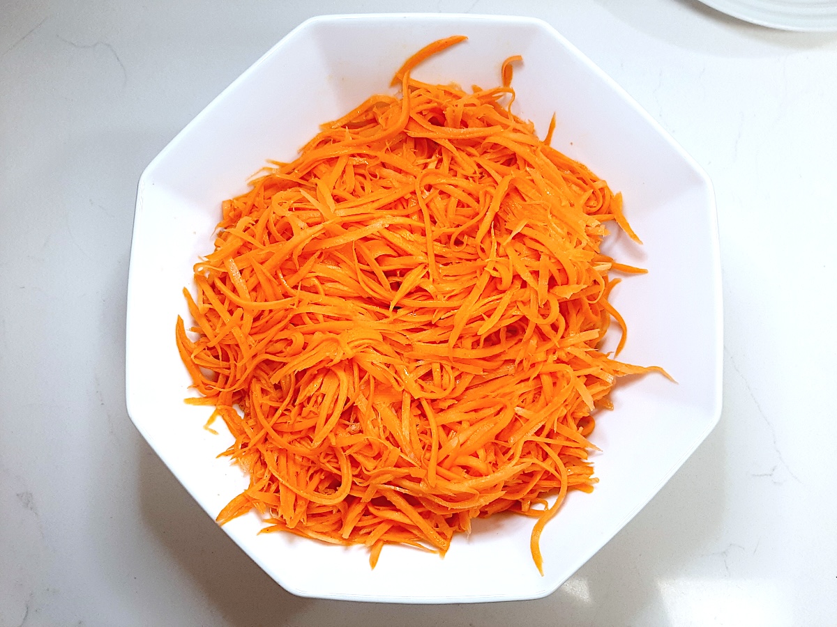 white bowl with thin strips of carrots in it on a white background